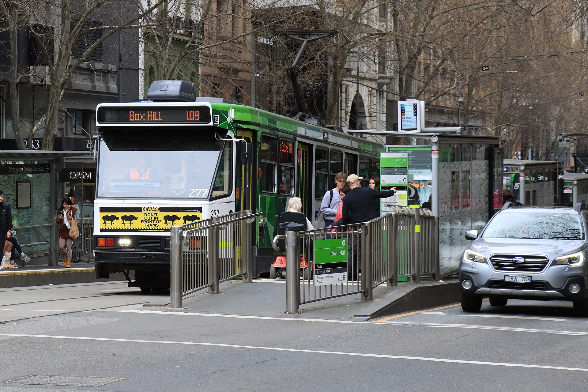 File:A class tram -277 in PTV livery operating a Route 109 service to Box Hill departing tram stop on Collins Street at Swanston Street while a person in a wheelchair waits for the next accessible tram in Melbourne.jpg
